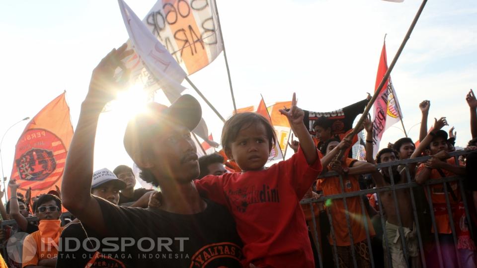 Seorang pria asik menggendong anaknya di acara ulang tahun Jakmania.